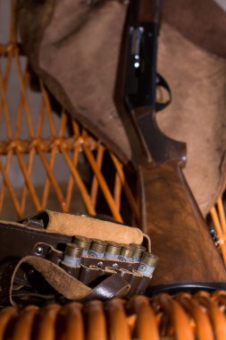 Fişek kemeri ve 12 kalibrelik av tüfeği sallanan sandalyede. Bir ayının derisi sallanan bir sandalyenin arkasında asılı.