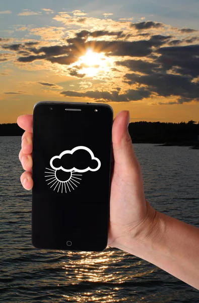 Smartphone in a female hand on a background of natural landscapes. Weather forecast image