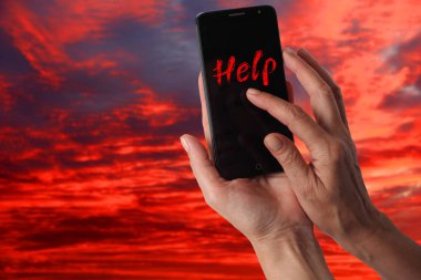 Dramatik fırtınalı gökyüzü bir arka plan üzerinde yardım için bir sinyal ile bir kadın elinde Smartphone