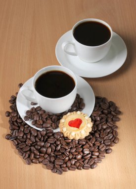 Ahşap mutfak masasında bir fincan kahve ve tatlı kurabiyeler.