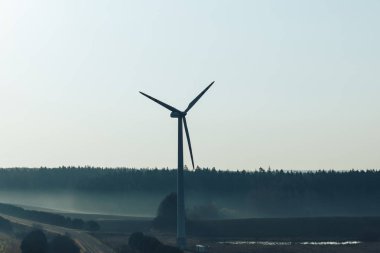 Silhouette of wind generator near empty road at sunrise 