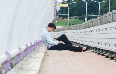 Köprüde tek başına oturmak ve aşağı bakıyor depresif genç