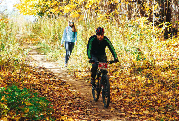 14 октября 2018 - Минск, Беларусь: 2018 Olympic Cross Country Cup XCO in Medvezhino, man riding mtb bicycle during race with female jogger behind

