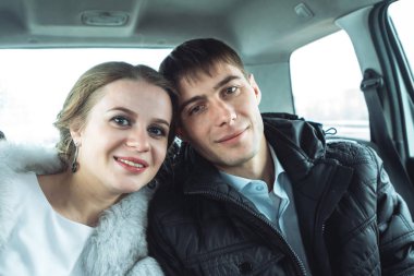 Gelin ve damat arabaya birlikte oturan ve kameraya bakıyor