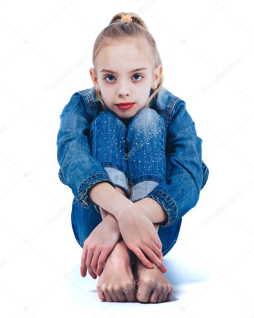 Young beautiful girl in denim suit sitting barefoot on white surface