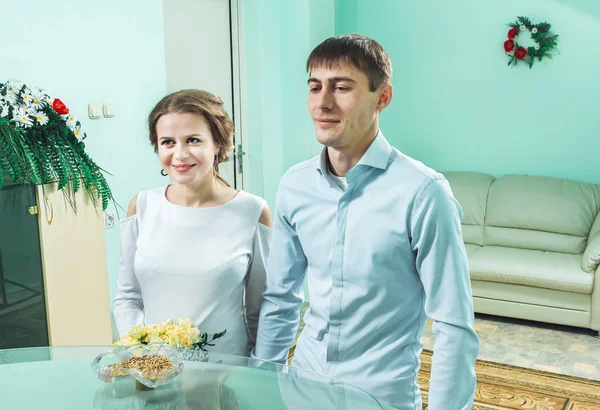 El novio en la camisa y la novia en un vestido blanco de pie delante de la mesa — Foto de Stock