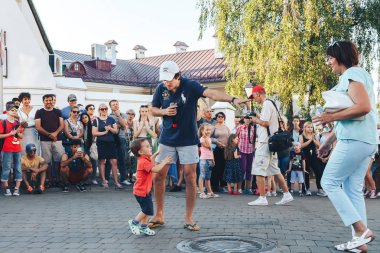 4 Ağustos 2018 Akşam kentte sokak şenlikleri Mikrofonlu bir adam küçük bir çocuğu gösterir annesinin meydanda insanların önünde olduğu yerde çocuğuyla bir sokak konserinde bir adam sahne alıyor
