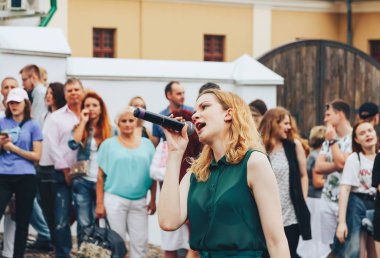 21 Temmuz 2018 , Minsk,Belarus Caddesi'nde yeşil takım elbiseli mikrofonla kız yürüyor bir sokak konserinde insanların önünde şarkı lar