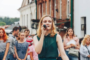 21 Temmuz 2018 , Minsk,Belarus Caddesi'nde yeşil takım elbiseli mikrofonla kız yürüyor bir sokak konserinde insanların önünde şarkı lar