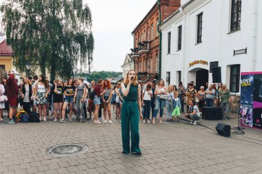 21 Temmuz 2018 , Minsk,Belarus Caddesi'nde yeşil takım elbiseli mikrofonla kız yürüyor bir sokak konserinde insanların önünde şarkı lar