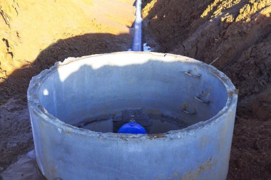 Boru hattı elemanları, plastik borular, beton kuyuda dökme demir vana. Plastik boru bir siperde kuyudan çıkıyor