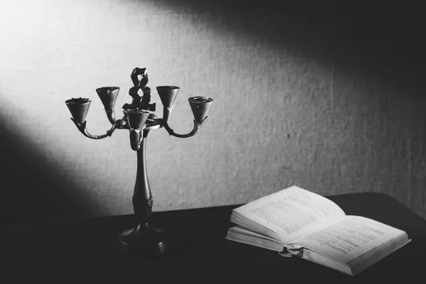 Een oude kandelaar staat in het donker in de buurt van een liggende boek. — Stockfoto