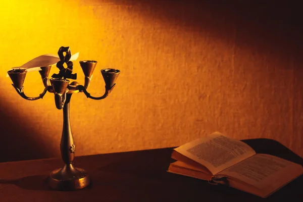 Een oude kandelaar staat in het donker in de buurt van een liggende boek. — Stockfoto