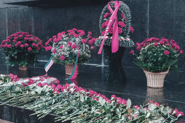 Baskets of flowers are next to the scattered flowers at the monument