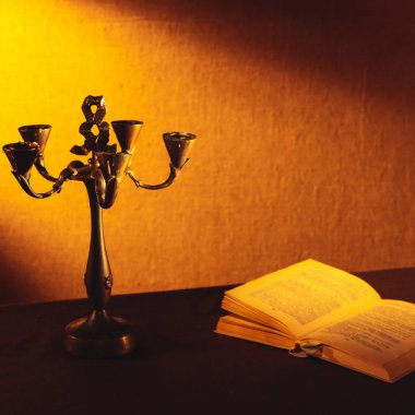 Eski bir mum çubuğu, uzanmış bir kitabın yanında bir ışık ışınının yanında karanlıkta duruyor..