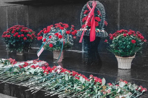 Baskets of flowers are next to the scattered flowers at the monument on the anniversary day