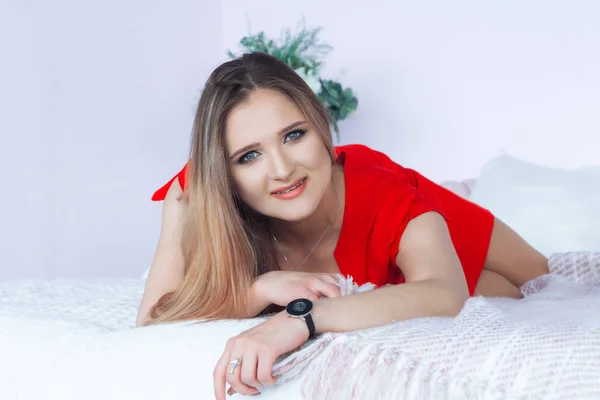 Beautiful girl in a red dress is lying on the bed — ストック写真