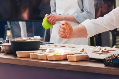 Şef portakal suyunu asistanın yanındaki yiyeceğe sıkıyor.