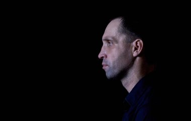 Siyah gömlekli, esmer, ciddi bir olgun adam.