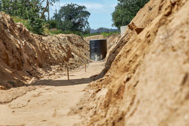 Su borularının düzleştirilmiş ve sıkıştırılmış bazlı kurulumu için siper. Güçlendirilmiş beton kuyu zift bazlı su geçirmez mastikle kaplı. Delik boru döşemek için açılmış.