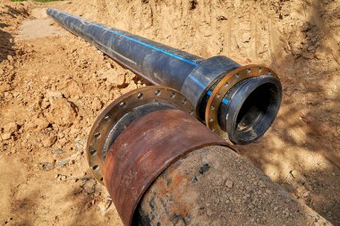 Kaynağı kaynaklı eski bir çelik su borusu su tedarik sistemini bağlamak için flanşlı yeni bir plastik borunun yanında yatıyor.