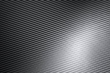 Endüstriyel karbon fiber kağıdının yapısal ayrıntıları tam çerçeve görünümünde ışık yüzeyde bir arkaplan dokusunda oynarken çapraz deseni gösterir