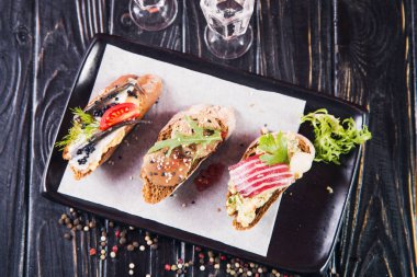 Bruschetta ringa balığı, ezme ve siyah ahşap arka plan üzerinde et ile