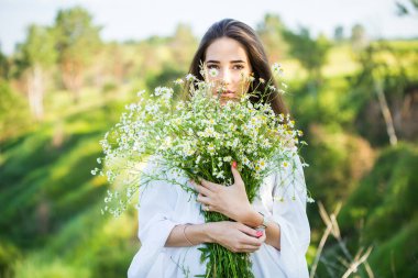 Dışarıda, çayırda elinde buketle güzel bir genç kızın portresi.