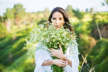 Dışarıda, çayırda elinde buketle güzel bir genç kızın portresi.
