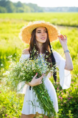 Şapkalı güzel bir genç kızın portresi, buketli, açık havada, tarlada.