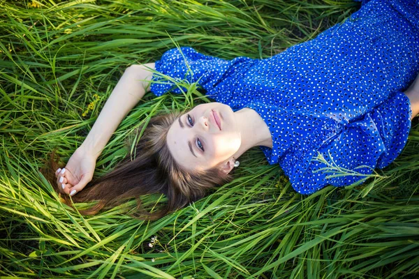 身穿蓝色衣服的年轻的欧洲姑娘躺在草地上 戴着一顶帽子 — 图库照片