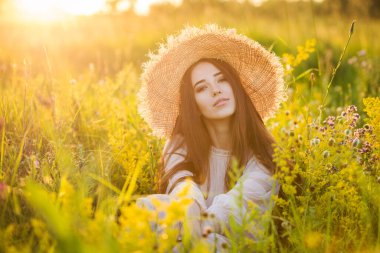 Genç, güzel Avrupalı kız batan güneşte, tarlada, şapkalı