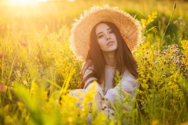 Genç, güzel Avrupalı kız batan güneşte, tarlada, şapkalı