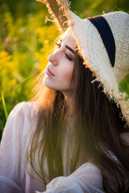 Genç, güzel Avrupalı kız batan güneşte, tarlada, şapkalı