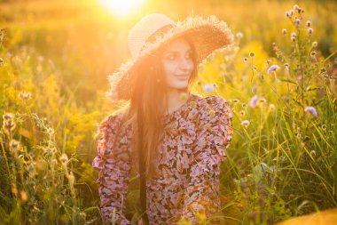 Genç, güzel Avrupalı kız batan güneşte, tarlada, şapkalı