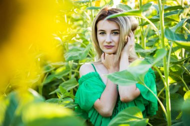 Doğada yeşil elbiseli, ayçiçekli sarışın bir kız.