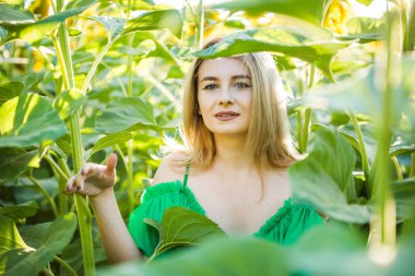 Doğada yeşil elbiseli, ayçiçekli sarışın bir kız.