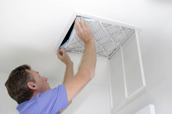 Putting In a New Air Filter, Guy placing into a square ceiling intake vent a clean white and blue air filter. As regular monthly maintenance a male puts in a new air filter in his ceiling air return.