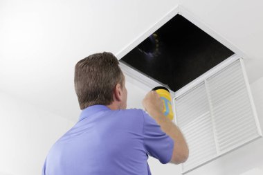 Adam bir hava kanalı bir el feneri ile teftiş. Hvac kanalları büyük bir kare delik içinde inceleyerek sarı bir el feneri ile büyük bir erkek. Erkek teknisyen bir ev hava girişi deliği içinde hava kanalları üzerinde seyir.
