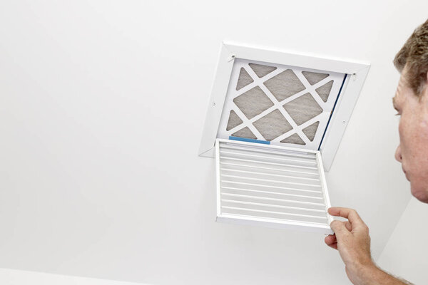 Man Opened a Vent to a Dirty Filter. Mature adult opening a small square HVAC air intake vent revealing a dirty air filter in the ceiling. Man opened a a vent grill cover to a dirty ceiling air filter