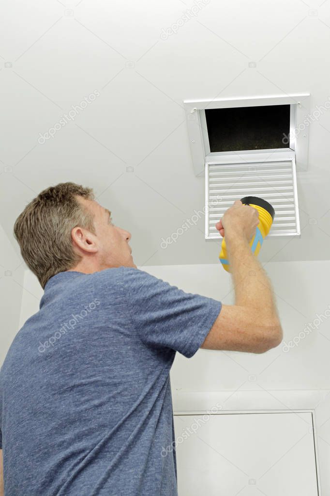 Person Examining Small Duct with a Flashlight. Homeowner looking into a small air duct searching for and dirt and examining the condition. Male examining the cleanliness of a small home HVAC air duct