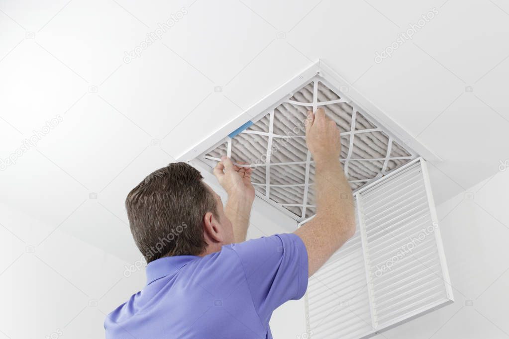 Person Removing Ceiling Air Filter. Caucasian male removing a square pleated dirty air filter with both hands from a ceiling air duct. Guy taking out an unclean air filter from a home ceiling air vent.