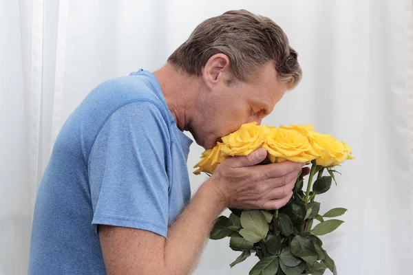 Mature man with his face in a yellow roses bunch. Yellow roses being held, smelled by an older man. One male sniffing a dozen yellow roses with tiny pink spots while holding them close up to his face