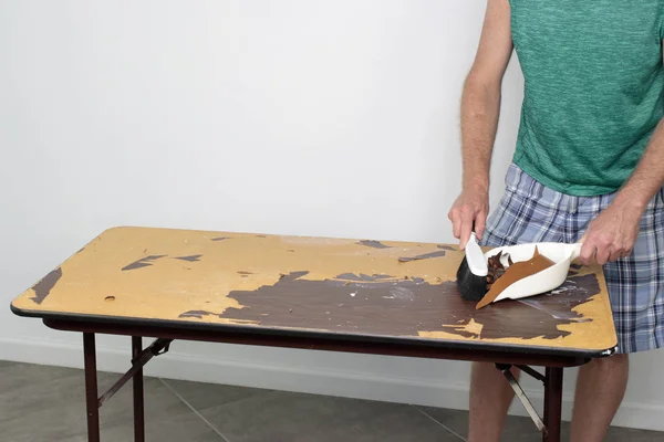 Male cleans off table he is preparing to resurface Male sweeping off a table with a dustpan and broom Guy cleaning old table top surface with dustpan and broom of garbage from preparing to resurface.