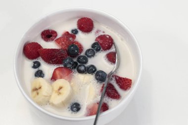 Muz, çilek, böğürtlen, ahududu, badem sütü ve Mısır gevreği beyaz kahvaltı kase. Sabah yemek karışık çilek, muz, badem sütü ve bir kaşık ile beyaz bir tabak içinde organik tahıl