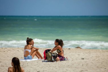 Miami Beach, Fl, Amerika Birleşik Devletleri - 12 Ekim 2016: İki kimliği belirsiz kadın South Beach kuma oturmak. 