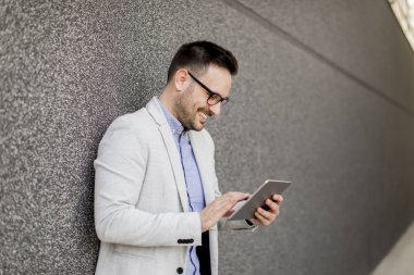 Gri duvar tarafından dijital tablet ile yakışıklı genç işadamı