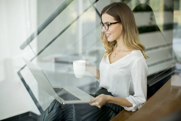 年轻妇女喝咖啡和工作在笔记本电脑在办公室 — 图库照片