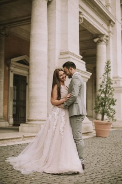 Yeni evli iki genç çekici yürüyor ve düğün günlerinde arka planda güzel ve antik mimari ile Roma'da poz