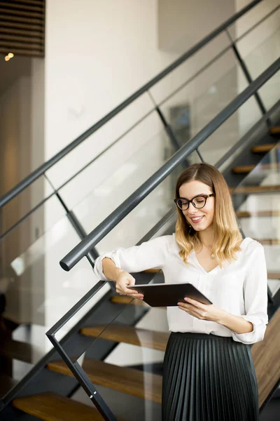 近代的なオフィスに立っている間デジタル タブレットに取り組んでいる若い魅力的な女性マネージャー — ストック写真